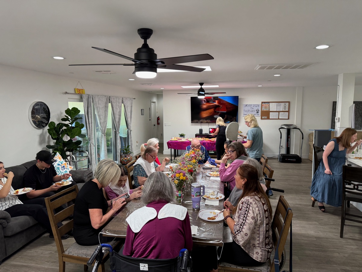 Family-style lunch at the dining table near the open kitchen, with caregivers and residents enjoying conversation